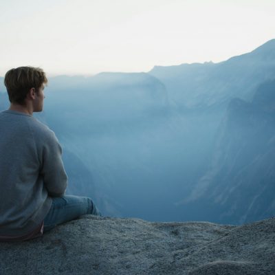 meditation man in gray shirt sits on cliff